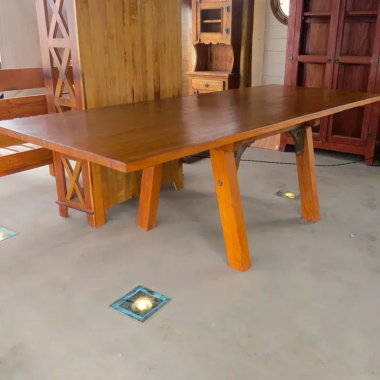 Mesa artesanal em peroba rosa, dimensões 2,50m x 1,00m, com feixe de réguas contínuas e detalhes em ferro fundido, capacidade para 8 lugares.